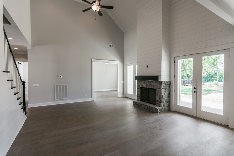 This is an example of a large country open concept living room in Nashville with grey walls, vinyl floors, a standard fireplace, a stone fireplace surround and brown floor.