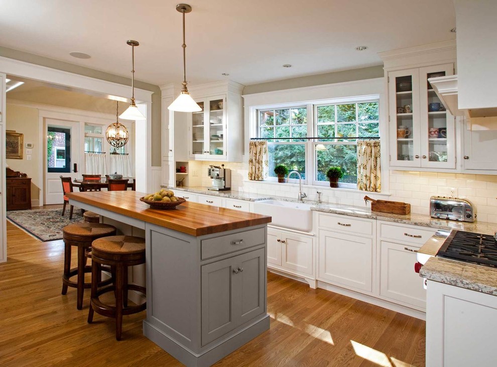 Design ideas for a large country l-shaped separate kitchen in Philadelphia with a farmhouse sink, shaker cabinets, white cabinets, wood benchtops, white splashback, stainless steel appliances, medium hardwood floors, with island, subway tile splashback and brown floor.