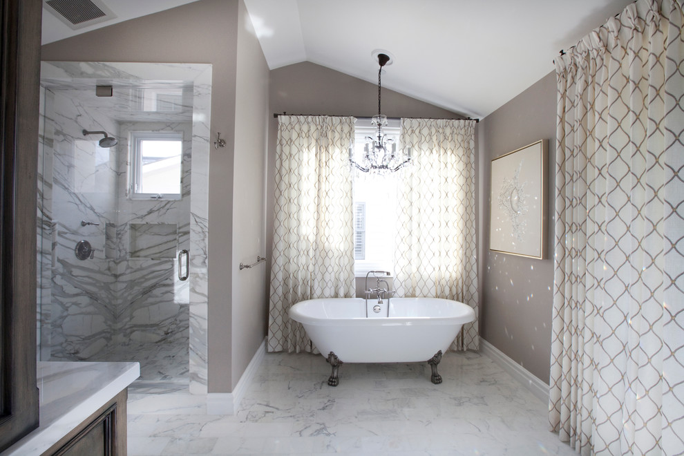 Example of a large transitional master gray tile, white tile and marble tile marble floor and white floor claw-foot bathtub design in Orange County with recessed-panel cabinets, medium tone wood cabinets, a one-piece toilet, a drop-in sink, marble countertops, brown walls, a hinged shower door and white countertops