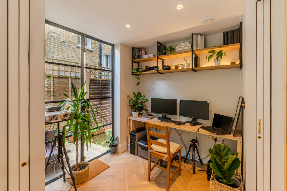 This is an example of a small contemporary home studio in London with grey walls, light hardwood flooring and a freestanding desk.
