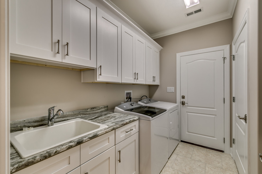 This is an example of a mid-sized traditional single-wall dedicated laundry room in Other with a drop-in sink, shaker cabinets, white cabinets, granite benchtops, beige walls, porcelain floors, a side-by-side washer and dryer, beige floor and grey benchtop.