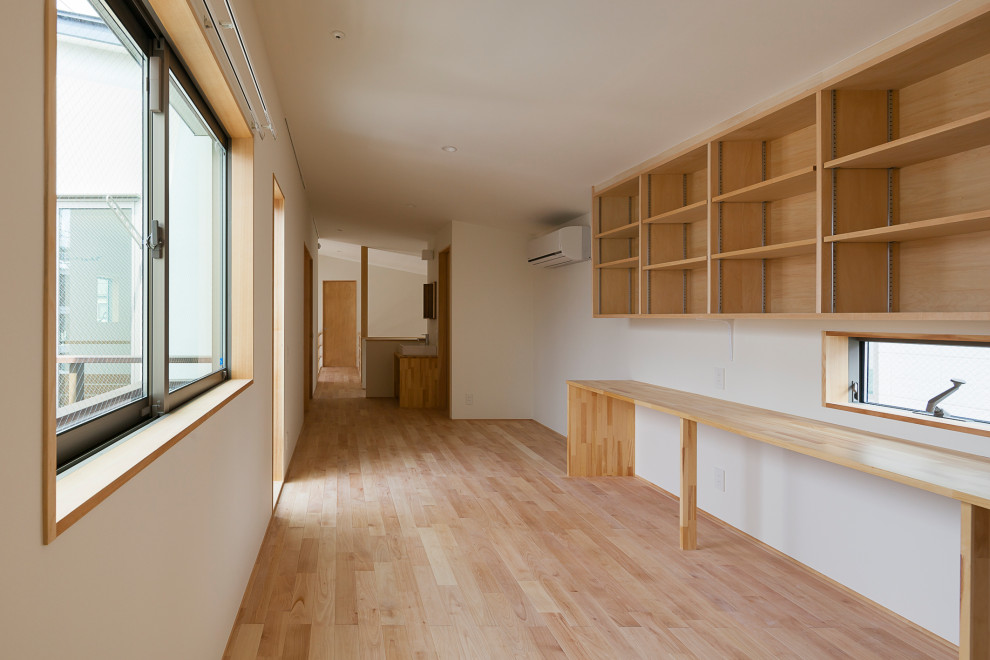 This is an example of a mid-sized home office in Tokyo with a library, white walls, light hardwood floors, a built-in desk, wallpaper and wallpaper.