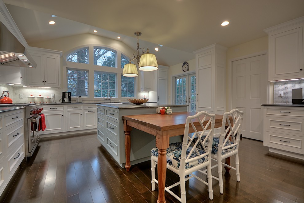 Mid-sized transitional u-shaped eat-in kitchen in New York with white cabinets, with island, granite benchtops, white splashback, glass tile splashback, stainless steel appliances, medium hardwood floors, a farmhouse sink and beaded inset cabinets.