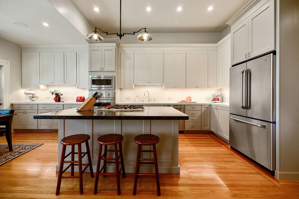 Photo of a mid-sized traditional l-shaped eat-in kitchen in San Francisco with an undermount sink, recessed-panel cabinets, white cabinets, white splashback, stainless steel appliances, with island, medium hardwood floors, brown floor and quartz benchtops.