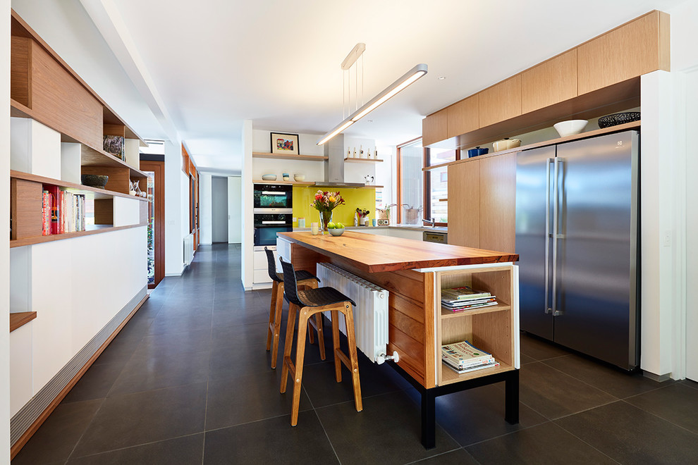 Photo of a midcentury kitchen in Melbourne with wood benchtops, yellow splashback, glass sheet splashback, stainless steel appliances, ceramic floors, with island and black floor.