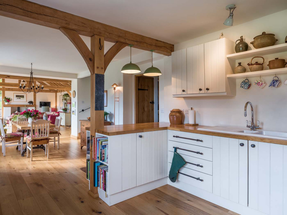 Country kitchen in Other with a drop-in sink, flat-panel cabinets, white cabinets, wood benchtops, medium hardwood floors, a peninsula, brown floor, brown benchtop and exposed beam.