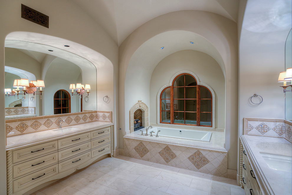 This is an example of an expansive traditional master bathroom in Phoenix with furniture-like cabinets, a vessel sink, light wood cabinets, a drop-in tub, beige tile, mosaic tile, beige walls, travertine floors and granite benchtops.