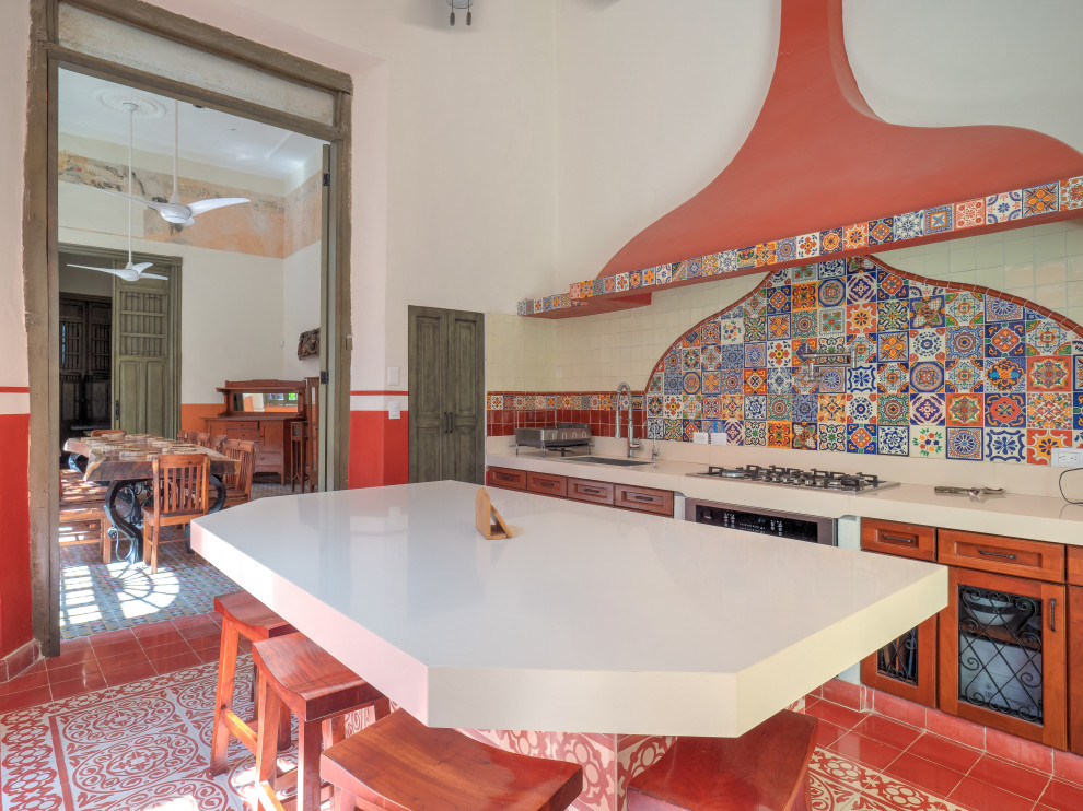 Photo of a mid-sized mediterranean u-shaped separate kitchen in Mexico City with an undermount sink, recessed-panel cabinets, medium wood cabinets, quartz benchtops, red splashback, mosaic tile splashback, stainless steel appliances, cement tiles, with island, red floor and white benchtop.