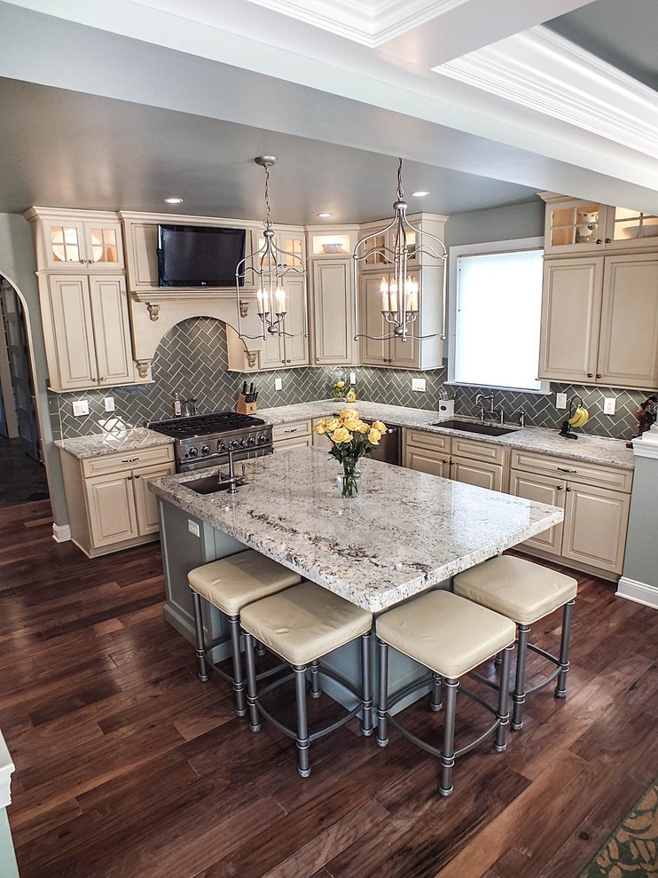 Photo of a large contemporary l-shaped eat-in kitchen in Cleveland with a drop-in sink, raised-panel cabinets, beige cabinets, granite benchtops, grey splashback, ceramic splashback, stainless steel appliances, dark hardwood floors and with island.