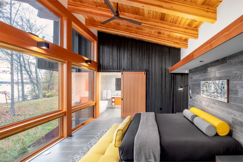 Cette photo montre une chambre parentale montagne en bois de taille moyenne avec un mur multicolore, un sol en carrelage de porcelaine, une cheminée double-face, un manteau de cheminée en béton, un sol gris et poutres apparentes.