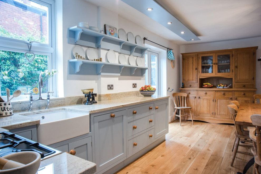 Large traditional l-shaped eat-in kitchen in Gloucestershire with a drop-in sink, shaker cabinets, blue cabinets, granite benchtops, brown splashback, stone slab splashback, stainless steel appliances, light hardwood floors, no island and white benchtop.