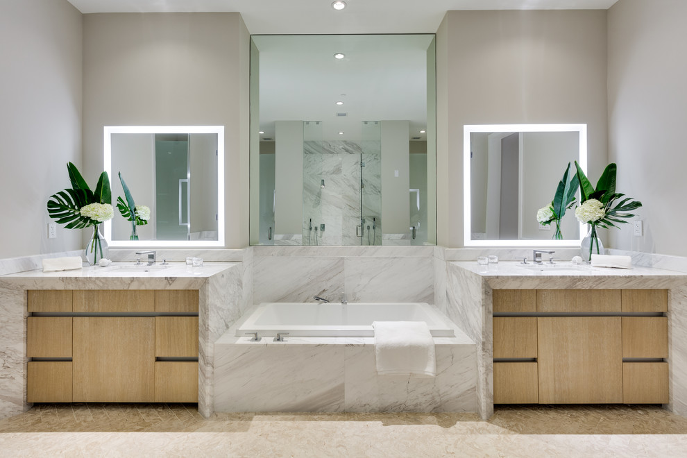 This is an example of a large contemporary master bathroom in Miami with flat-panel cabinets, light wood cabinets, grey walls, an undermount sink, marble benchtops, beige floor, white benchtops and a drop-in tub.