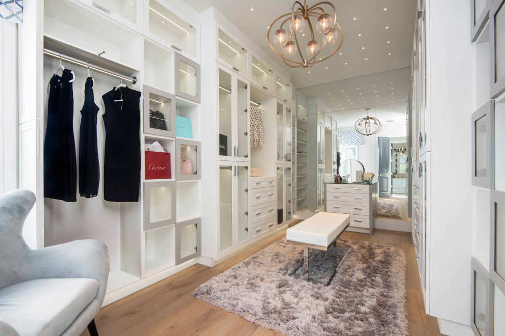 Photo of a transitional women's walk-in wardrobe in Tampa with glass-front cabinets, white cabinets, medium hardwood floors and brown floor.