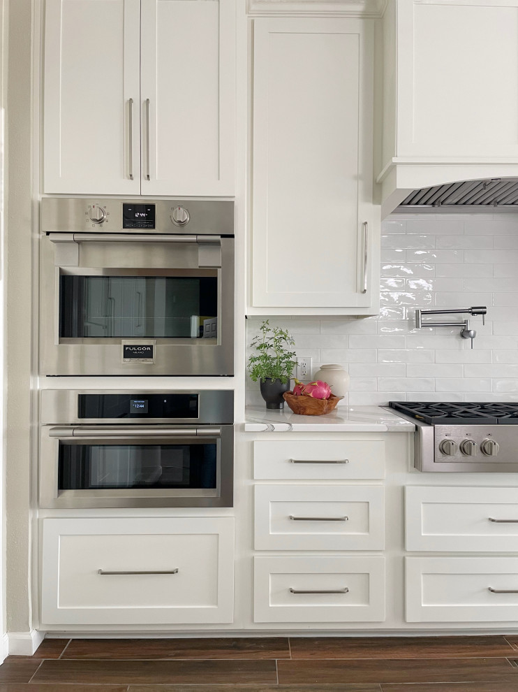 Example of a large ceramic tile and brown floor kitchen design in Austin with an undermount sink, shaker cabinets, white cabinets, white backsplash, subway tile backsplash, stainless steel appliances, an island and white countertops