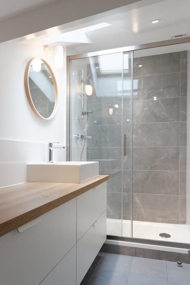 Photo of a small scandinavian master bathroom in Paris with flat-panel cabinets, white cabinets, a curbless shower, a two-piece toilet, gray tile, stone tile, white walls, concrete floors, a drop-in sink and wood benchtops.