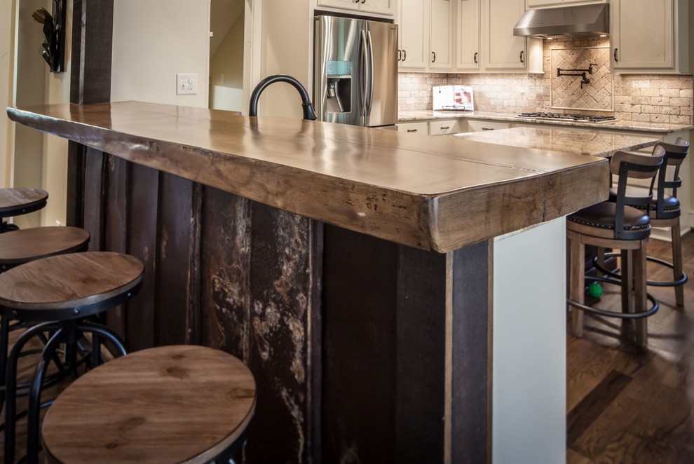 Example of a mid-sized transitional u-shaped medium tone wood floor and brown floor eat-in kitchen design with a farmhouse sink, recessed-panel cabinets, white cabinets, granite countertops, beige backsplash, ceramic backsplash, stainless steel appliances and an island