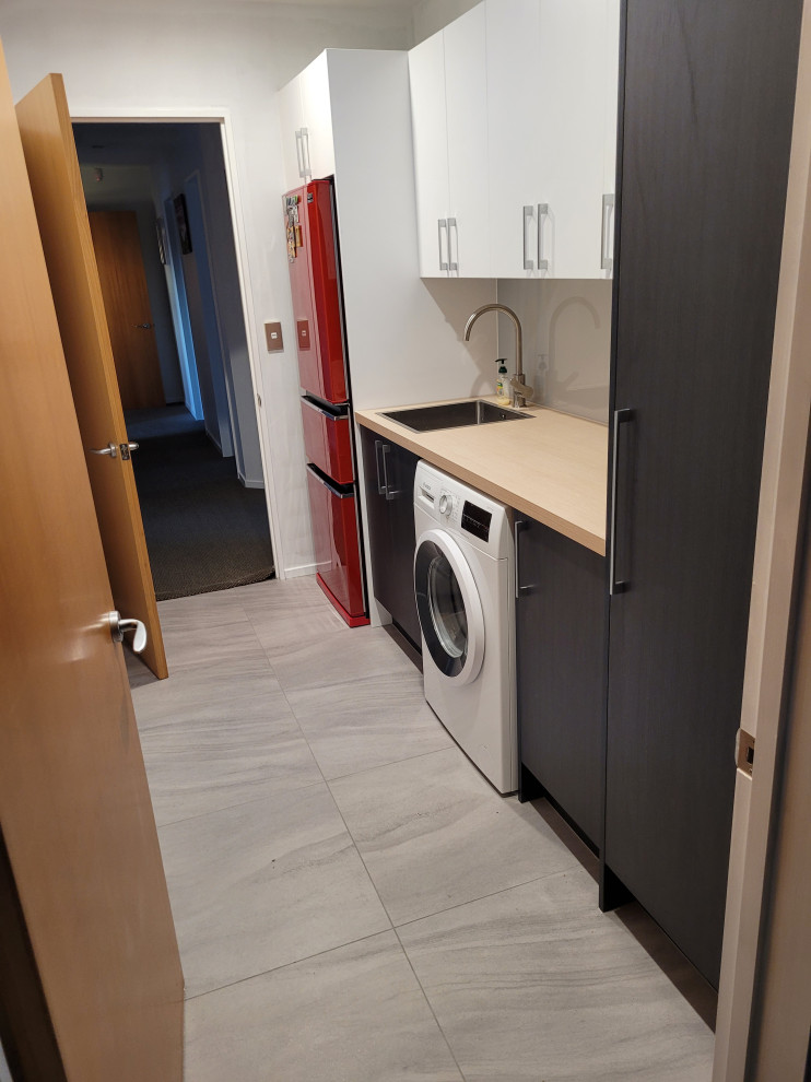 This is an example of a mid-sized single-wall utility room in Other with a drop-in sink, flat-panel cabinets, dark wood cabinets, laminate benchtops, grey splashback, glass sheet splashback, white walls, ceramic floors, a side-by-side washer and dryer, grey floor and beige benchtop.