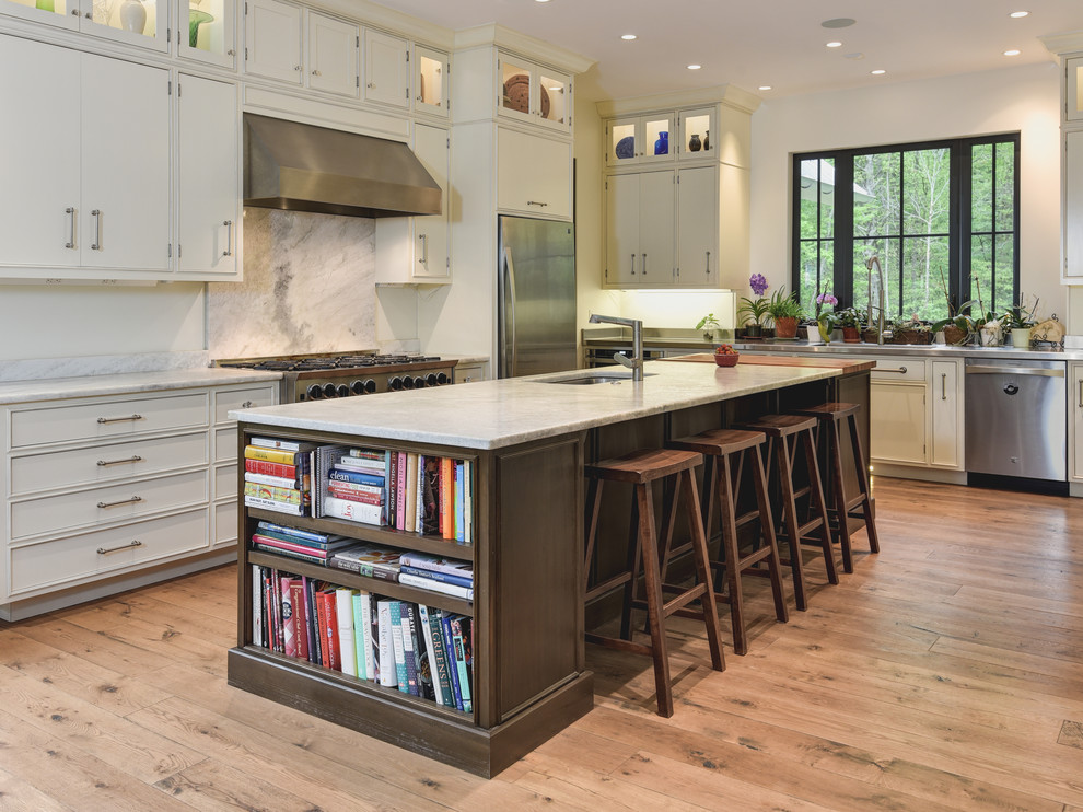 Photo of a country l-shaped kitchen in Other with an undermount sink, recessed-panel cabinets, grey cabinets, white splashback, stone slab splashback, stainless steel appliances, medium hardwood floors, with island and brown floor.