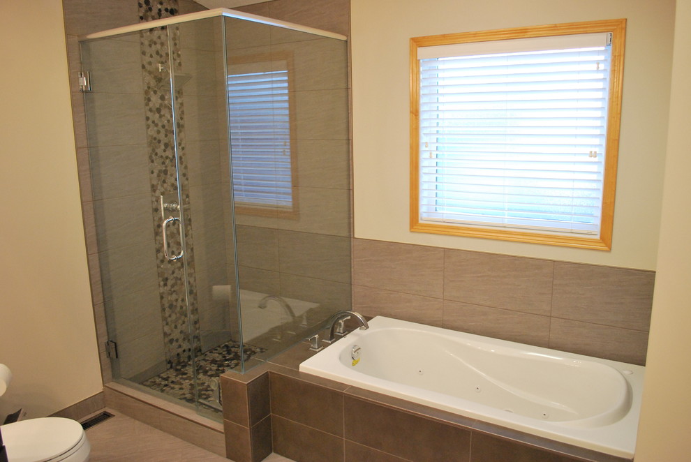 This is an example of a mid-sized traditional master bathroom in Calgary with shaker cabinets, dark wood cabinets, a drop-in tub, a corner shower, a two-piece toilet, multi-coloured tile, pebble tile, beige walls, laminate floors, an undermount sink, solid surface benchtops, beige floor and a hinged shower door.