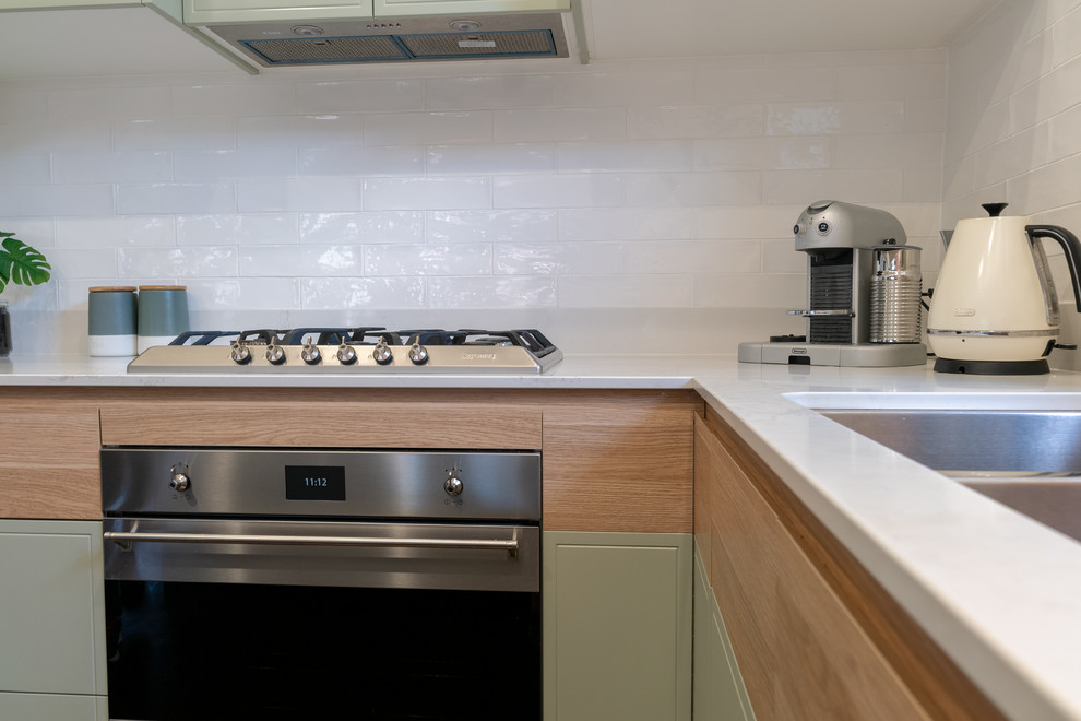 This is an example of a mid-sized eclectic u-shaped eat-in kitchen in Newcastle - Maitland with an undermount sink, flat-panel cabinets, green cabinets, quartz benchtops, white splashback, subway tile splashback, stainless steel appliances, light hardwood floors, a peninsula, brown floor and white benchtop.