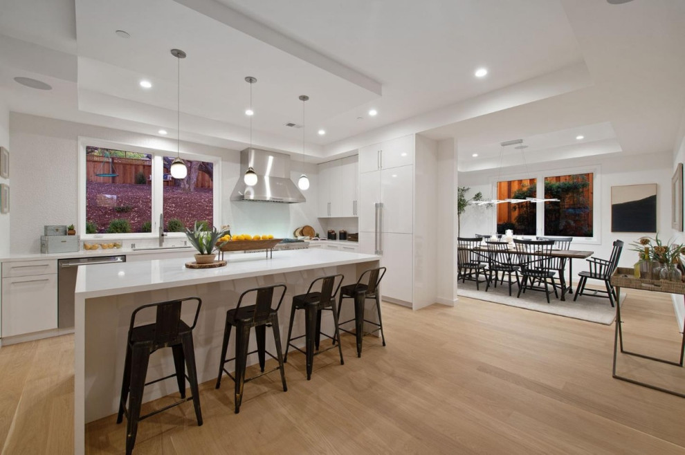 Photo of a mid-sized modern l-shaped eat-in kitchen in San Francisco with an undermount sink, flat-panel cabinets, white cabinets, quartz benchtops, white splashback, porcelain splashback, stainless steel appliances, medium hardwood floors, with island, yellow floor and white benchtop.