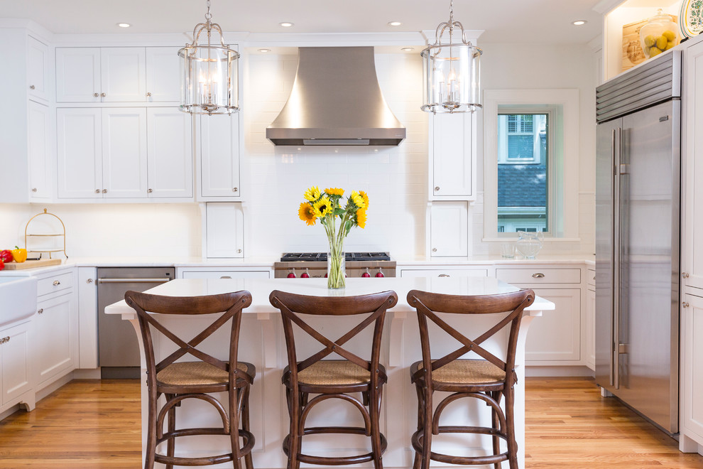 Mid-sized transitional u-shaped medium tone wood floor eat-in kitchen photo in Cincinnati with a farmhouse sink, recessed-panel cabinets, white cabinets, marble countertops, white backsplash, subway tile backsplash, stainless steel appliances and an island