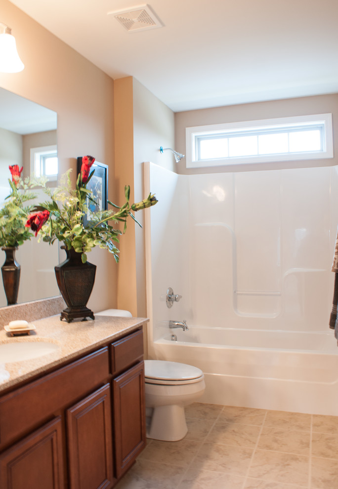 Inspiration for a traditional bathroom in Other with an undermount sink, raised-panel cabinets, medium wood cabinets, granite benchtops, an alcove tub, a shower/bathtub combo, a one-piece toilet, beige tile, ceramic tile, beige walls and ceramic floors.