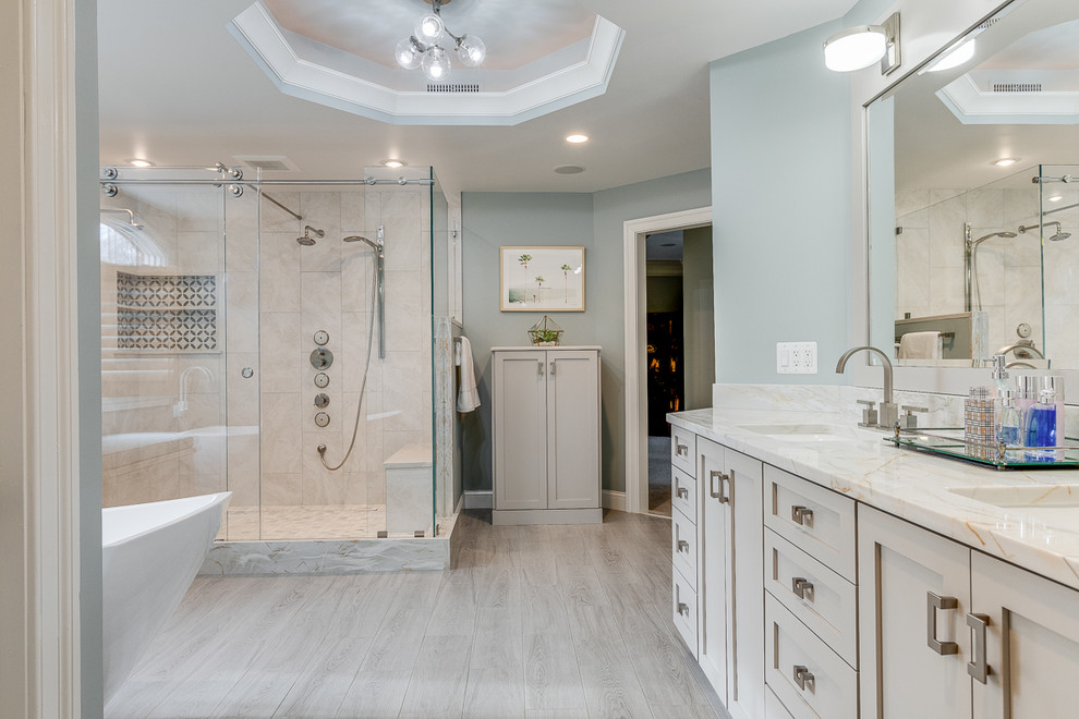Large transitional master bathroom in DC Metro with shaker cabinets, grey cabinets, a freestanding tub, a double shower, a two-piece toilet, gray tile, porcelain tile, blue walls, porcelain floors, an undermount sink, quartzite benchtops, grey floor, a sliding shower screen and grey benchtops.