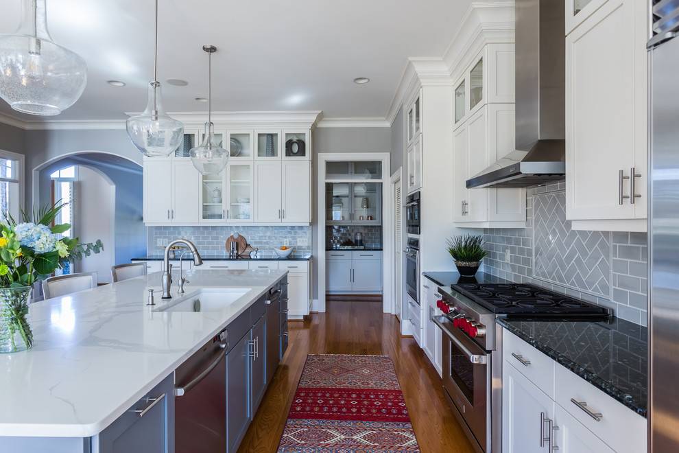 Inspiration for a transitional galley kitchen remodel with an undermount sink, shaker cabinets, white cabinets, gray backsplash, subway tile backsplash, stainless steel appliances, an island and white countertops