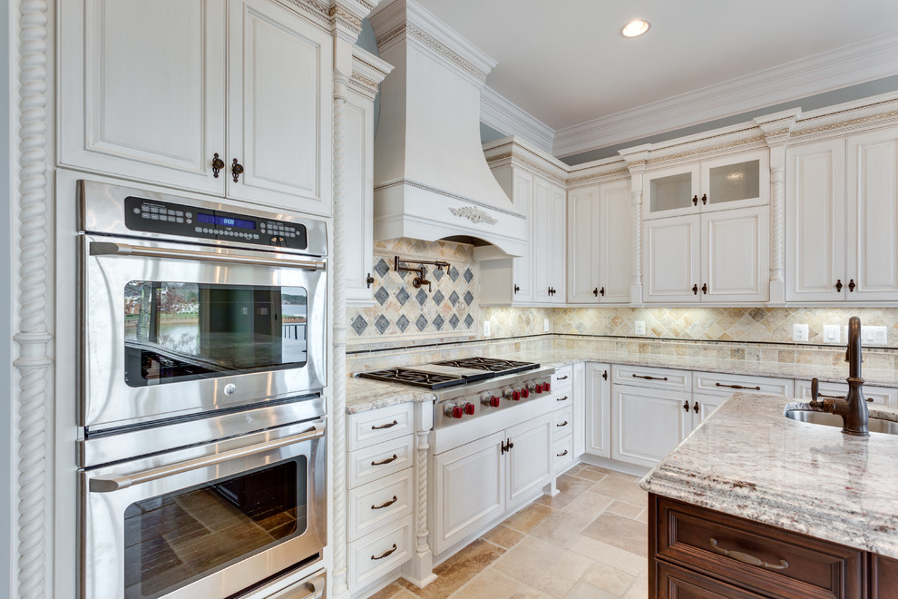Inspiration for a large l-shaped kitchen in Raleigh with an undermount sink, raised-panel cabinets, white cabinets, granite benchtops, beige splashback, ceramic splashback, stainless steel appliances, travertine floors, with island and beige floor.