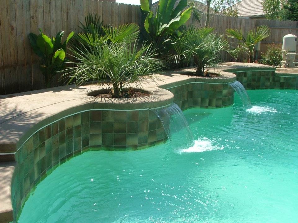 Large tropical backyard custom-shaped pool in Other with a water feature and stamped concrete.