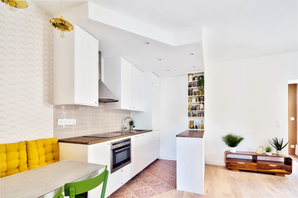 Inspiration for a mid-sized traditional galley open plan kitchen in Paris with an undermount sink, flat-panel cabinets, white cabinets, wood benchtops, pink splashback, ceramic splashback, stainless steel appliances, terra-cotta floors and with island.