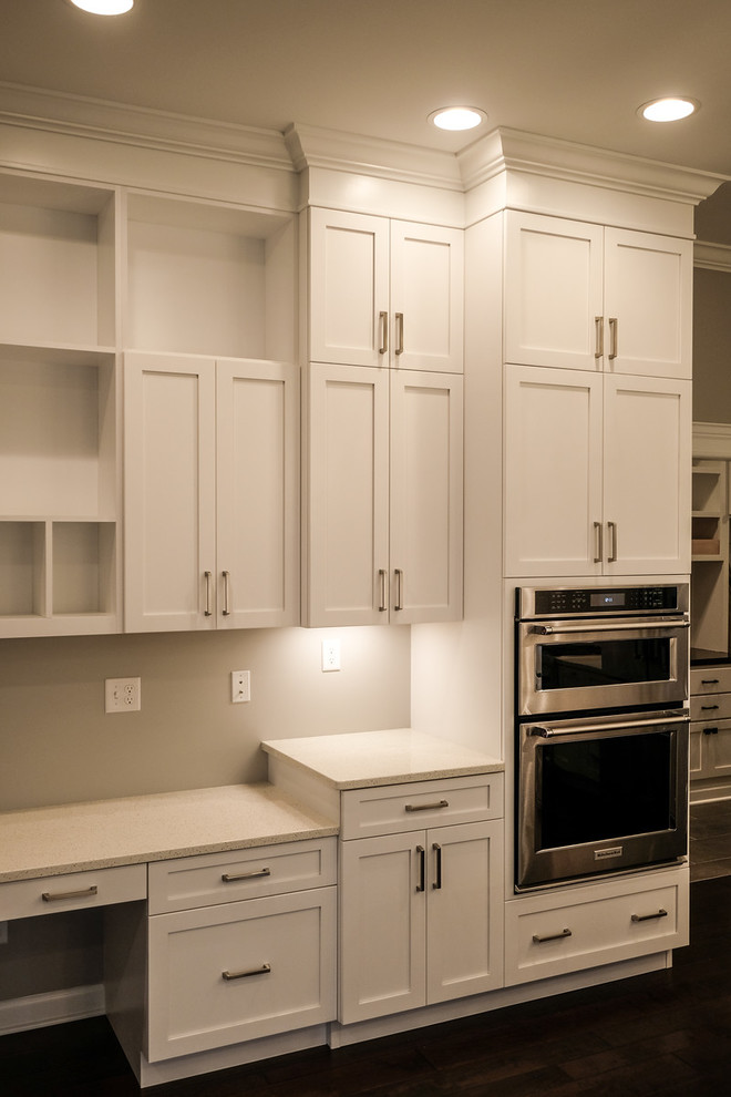 Inspiration for a large transitional u-shaped dark wood floor and brown floor eat-in kitchen remodel with a farmhouse sink, recessed-panel cabinets, white cabinets, quartz countertops, white backsplash, stainless steel appliances, an island and white countertops