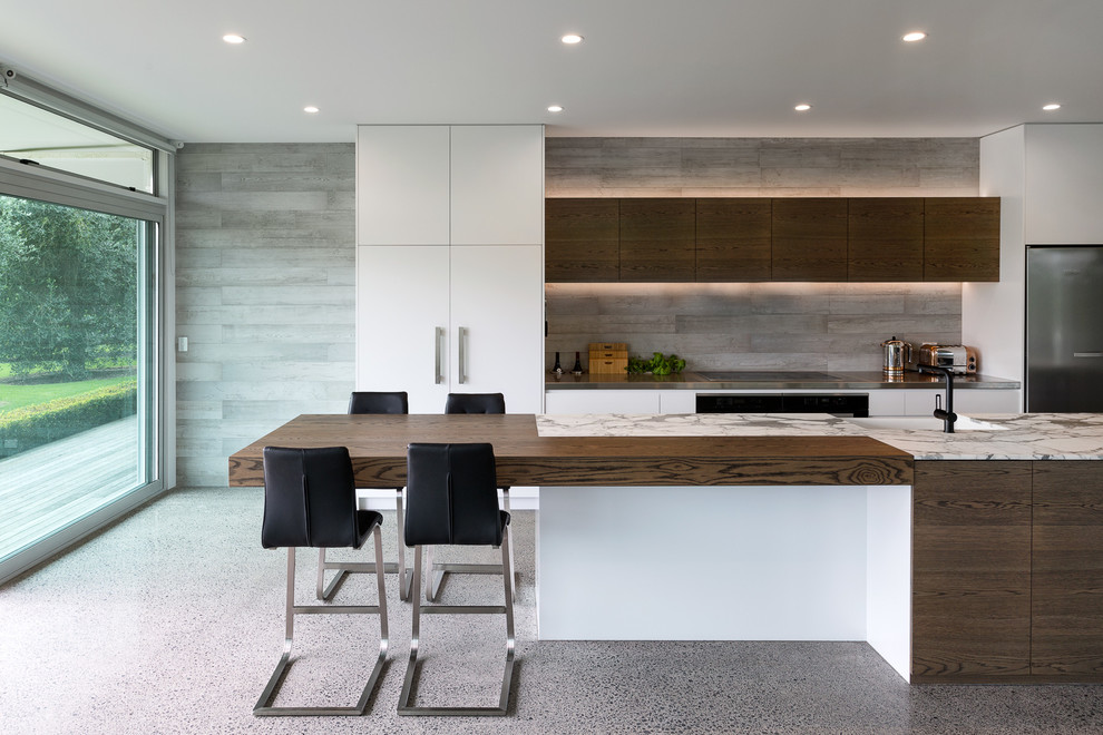 Photo of a contemporary kitchen in Auckland with a farmhouse sink, dark wood cabinets, stainless steel benchtops, grey splashback, stainless steel appliances and with island.