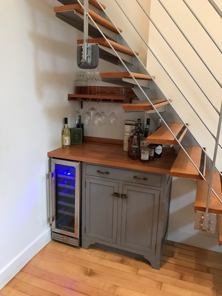 This is an example of a small contemporary single-wall home bar in New York with no sink, grey cabinets, wood benchtops, white splashback and bamboo floors.