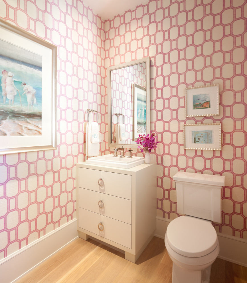 Design ideas for a small traditional powder room in Minneapolis with flat-panel cabinets, white cabinets, pink walls, light hardwood floors, a two-piece toilet and a vessel sink.