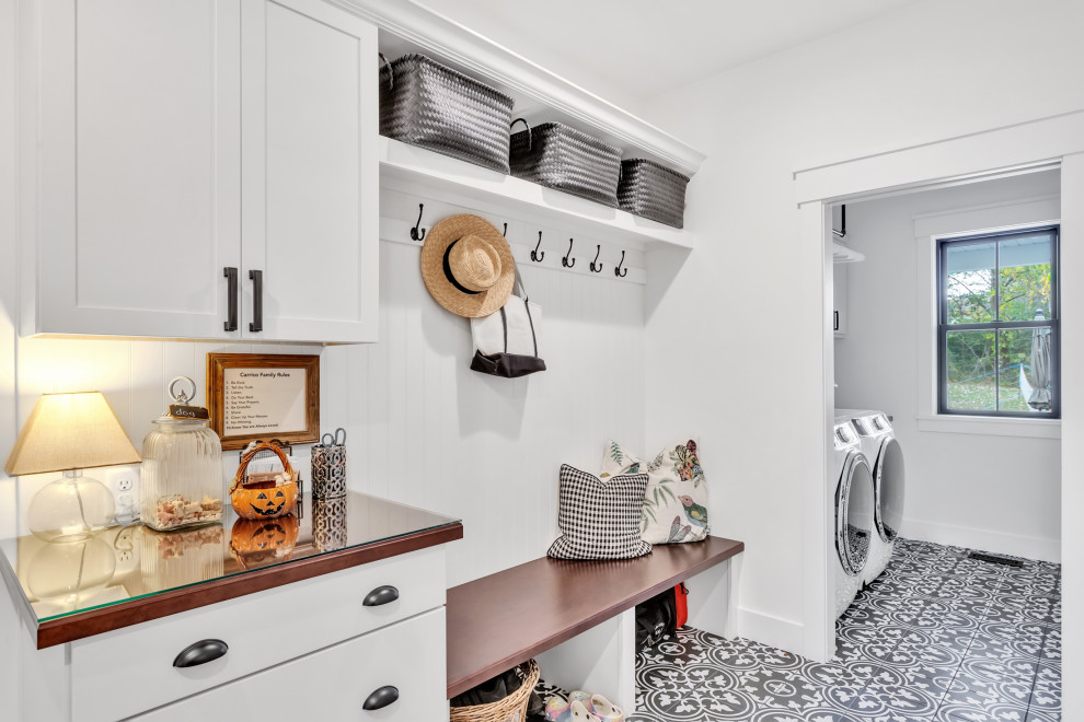 This is an example of a large arts and crafts single-wall utility room in Other with a drop-in sink, shaker cabinets, white cabinets, wood benchtops, white splashback, shiplap splashback, white walls, porcelain floors, a side-by-side washer and dryer, black floor, brown benchtop and panelled walls.