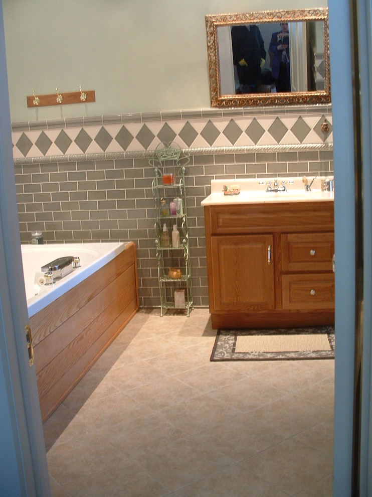 Photo of a large traditional 3/4 bathroom in Philadelphia with raised-panel cabinets, light wood cabinets, a drop-in tub, gray tile, porcelain tile, grey walls, ceramic floors and an integrated sink.