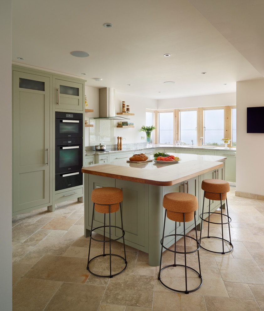 This is an example of a large beach style l-shaped open plan kitchen in Essex with with island, shaker cabinets, green cabinets and black appliances.