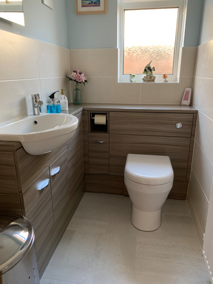 This is an example of a small contemporary 3/4 bathroom in Sussex with flat-panel cabinets, medium wood cabinets, a corner shower, a wall-mount toilet, beige tile, porcelain tile, blue walls, vinyl floors, an integrated sink, wood benchtops, beige floor, a sliding shower screen, brown benchtops, an enclosed toilet, a single vanity and a built-in vanity.