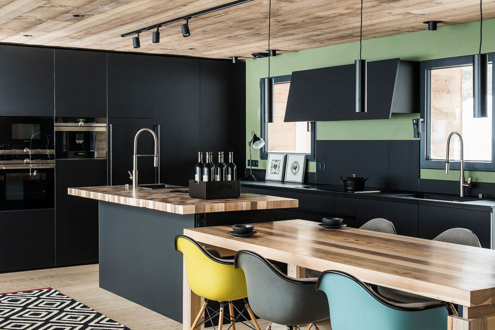 Photo of a mid-sized contemporary galley eat-in kitchen in Lyon with a drop-in sink, flat-panel cabinets, beige cabinets, wood benchtops, black splashback, black appliances, light hardwood floors, with island, beige floor and brown benchtop.