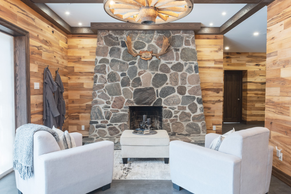 Example of a large mountain style walk-out vinyl floor, gray floor, exposed beam and wood wall basement design with a bar, multicolored walls, a standard fireplace and a stone fireplace
