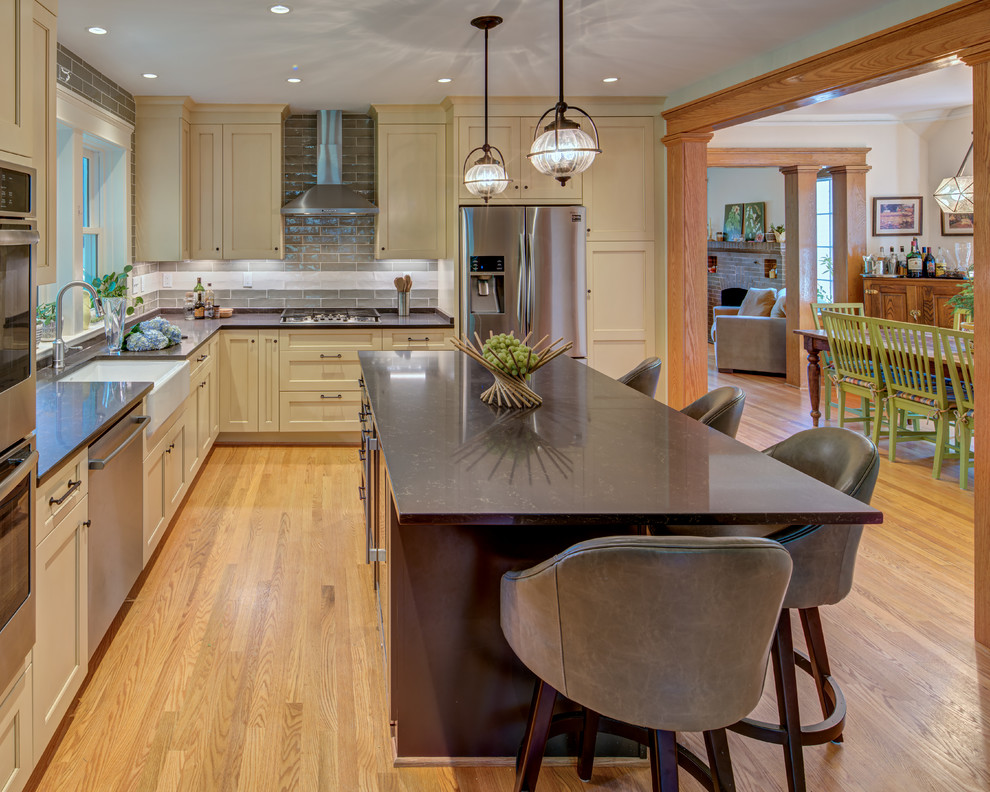 Design ideas for a large country l-shaped open plan kitchen in DC Metro with a farmhouse sink, shaker cabinets, beige cabinets, quartz benchtops, green splashback, subway tile splashback, stainless steel appliances, light hardwood floors, with island, yellow floor and grey benchtop.
