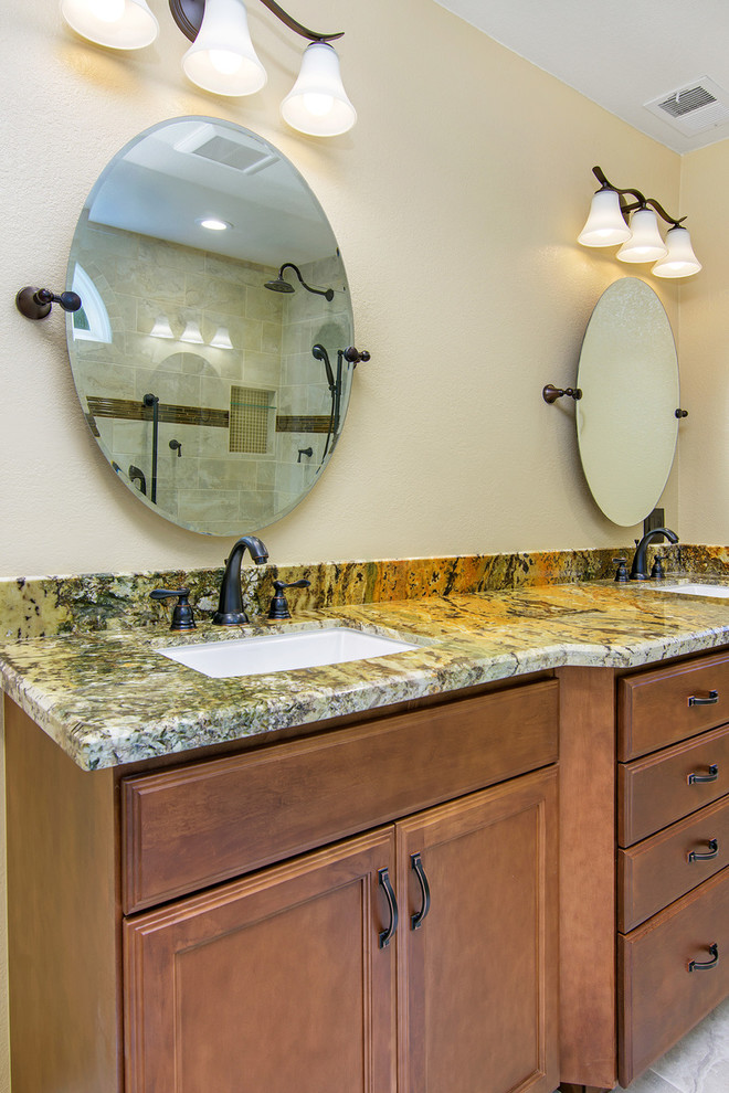 Photo of a large traditional master bathroom in San Diego with recessed-panel cabinets, medium wood cabinets, a curbless shower, a two-piece toilet, beige tile, ceramic tile, beige walls, travertine floors, granite benchtops, an undermount sink, an open shower, beige benchtops, a double vanity and a built-in vanity.