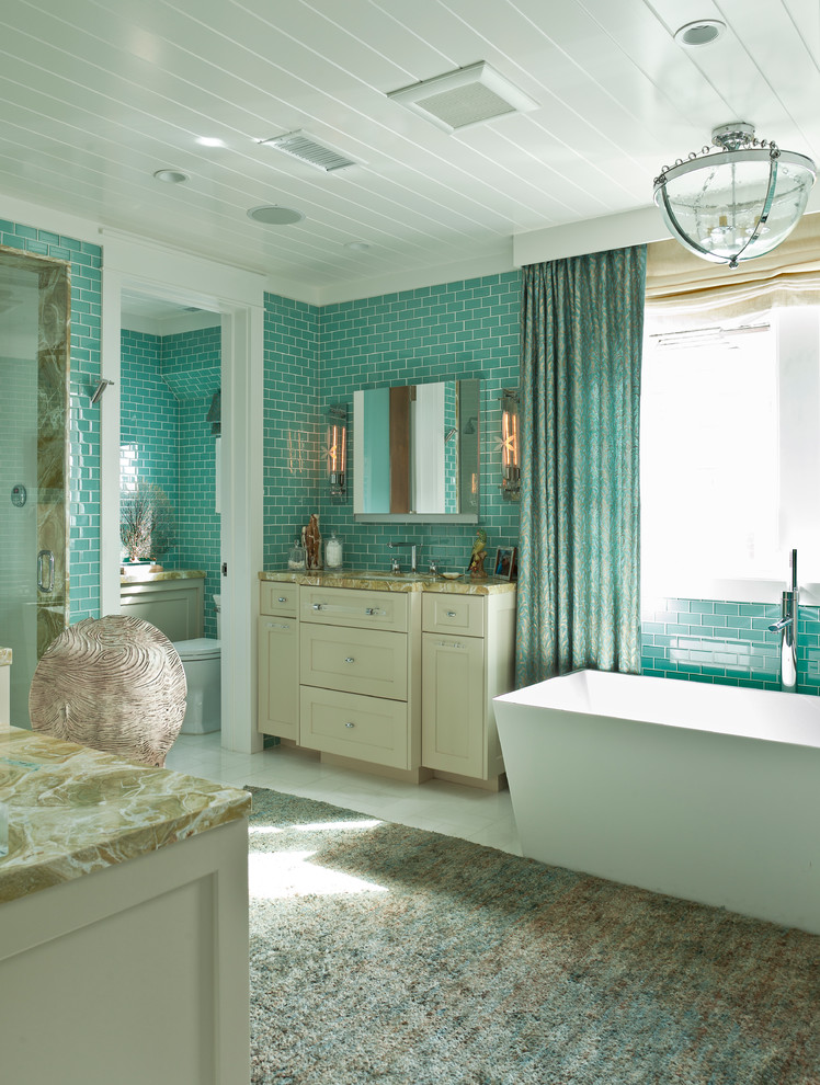 Photo of an expansive beach style master bathroom in Orange County with recessed-panel cabinets, beige cabinets, an undermount tub, a shower/bathtub combo, a two-piece toilet, blue tile, blue walls, a console sink, onyx benchtops, multi-coloured benchtops, subway tile, a hinged shower door, porcelain floors and white floor.