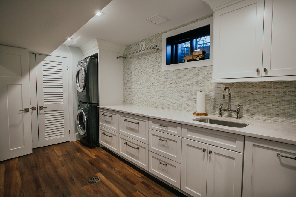 Design ideas for an expansive transitional single-wall dedicated laundry room in Denver with an undermount sink, shaker cabinets, white cabinets, quartz benchtops, grey walls, vinyl floors, a stacked washer and dryer, brown floor and white benchtop.