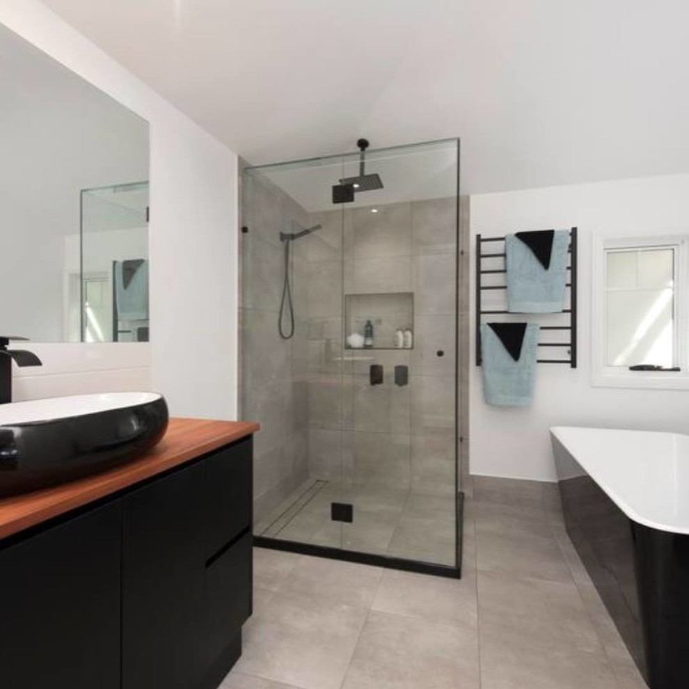Mid-sized modern master bathroom in Brisbane with furniture-like cabinets, black cabinets, a freestanding tub, a corner shower, gray tile, ceramic tile, white walls, ceramic floors, an integrated sink, wood benchtops, grey floor, a hinged shower door and white benchtops.