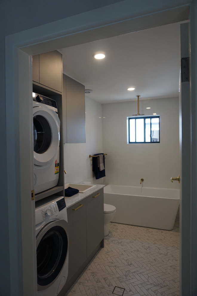 Design ideas for a small contemporary l-shaped utility room in Sydney with a single-bowl sink, flat-panel cabinets, grey cabinets, quartz benchtops, white walls, porcelain floors, a stacked washer and dryer, multi-coloured floor and multi-coloured benchtop.