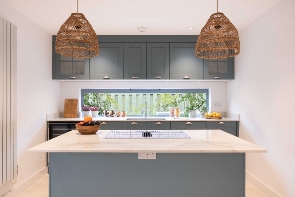 Inspiration for a medium sized contemporary grey and white kitchen/diner in Gloucestershire with an integrated sink, shaker cabinets, blue cabinets, engineered stone countertops, integrated appliances, porcelain flooring, an island, beige floors and white worktops.