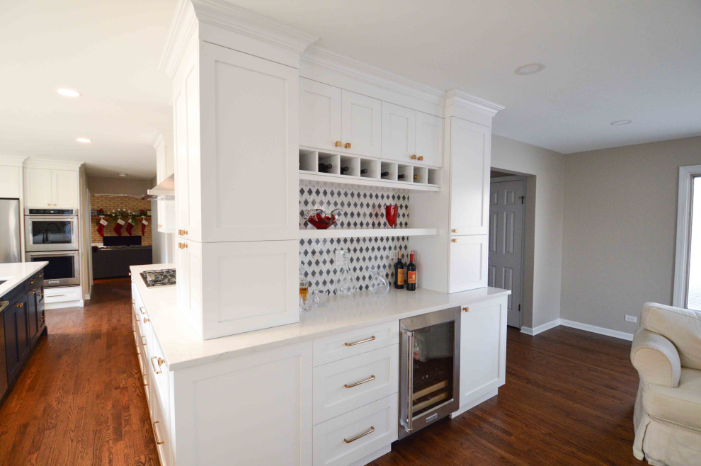 This is an example of a large transitional eat-in kitchen in Chicago with white cabinets, quartz benchtops, white splashback, stainless steel appliances, medium hardwood floors, with island and white benchtop.